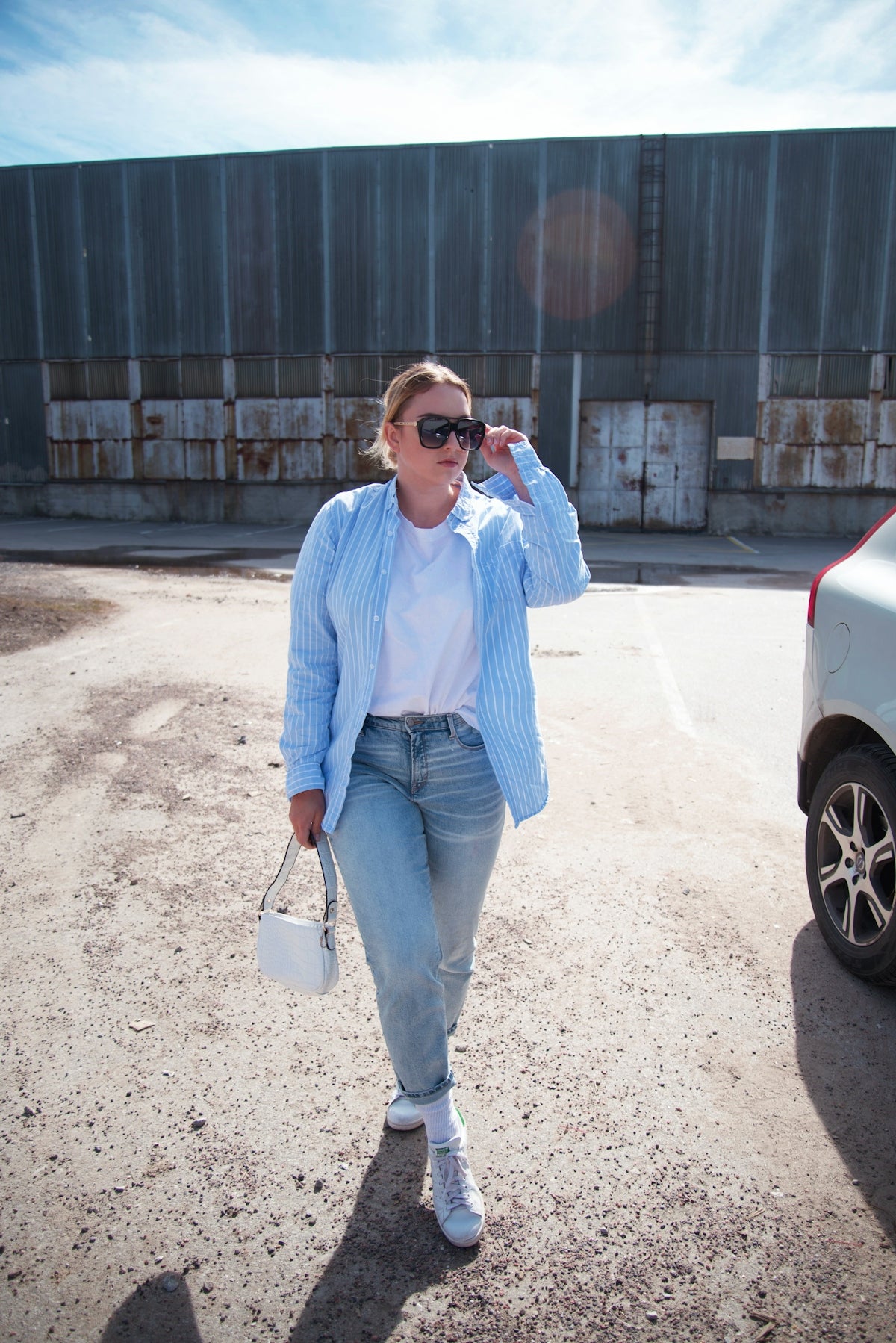 a woman walking in a parking lot holding a white purse